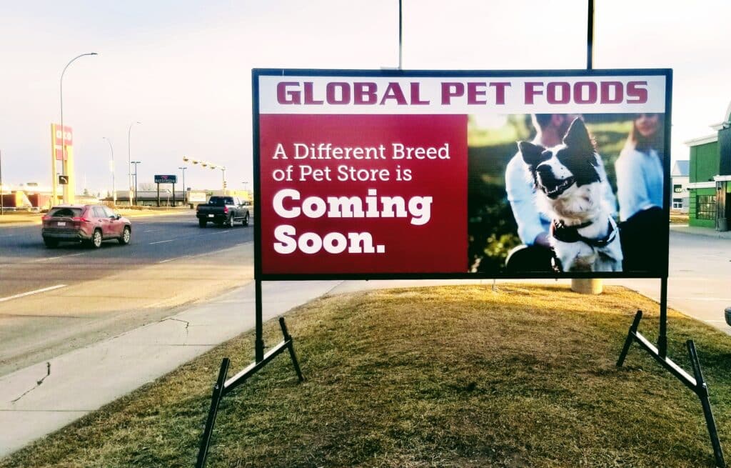 A temporary portable LED sign with an image of a dog on it. Words say Global Pet Foods. A different breed of pet store is coming soon. 
