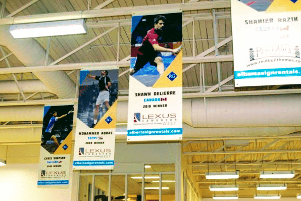 Banners hang from the rafters of a gymnasium with a white ceiling, commemorating the achievements of different athletes.
